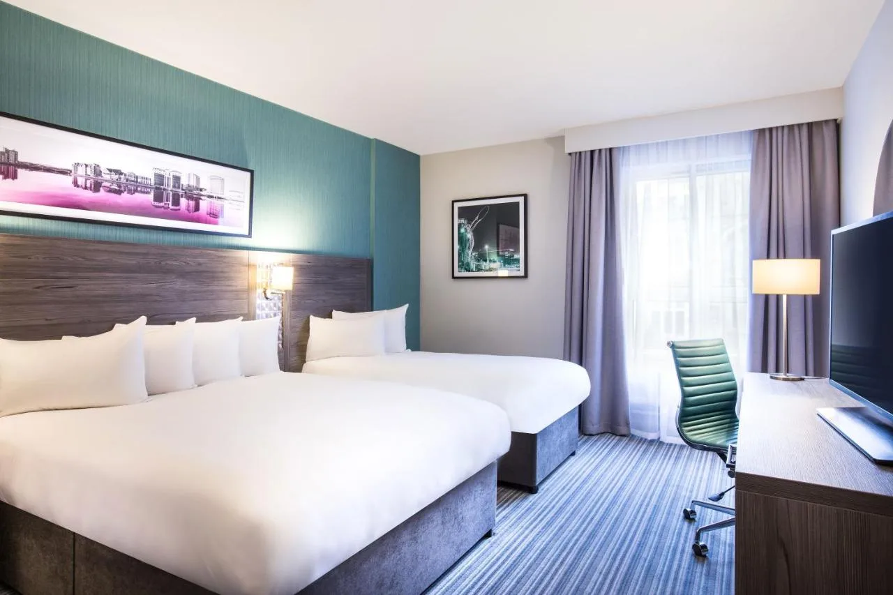 a hotel room with two beds and a desk at Leonardo Hotel Belfast in Belfast